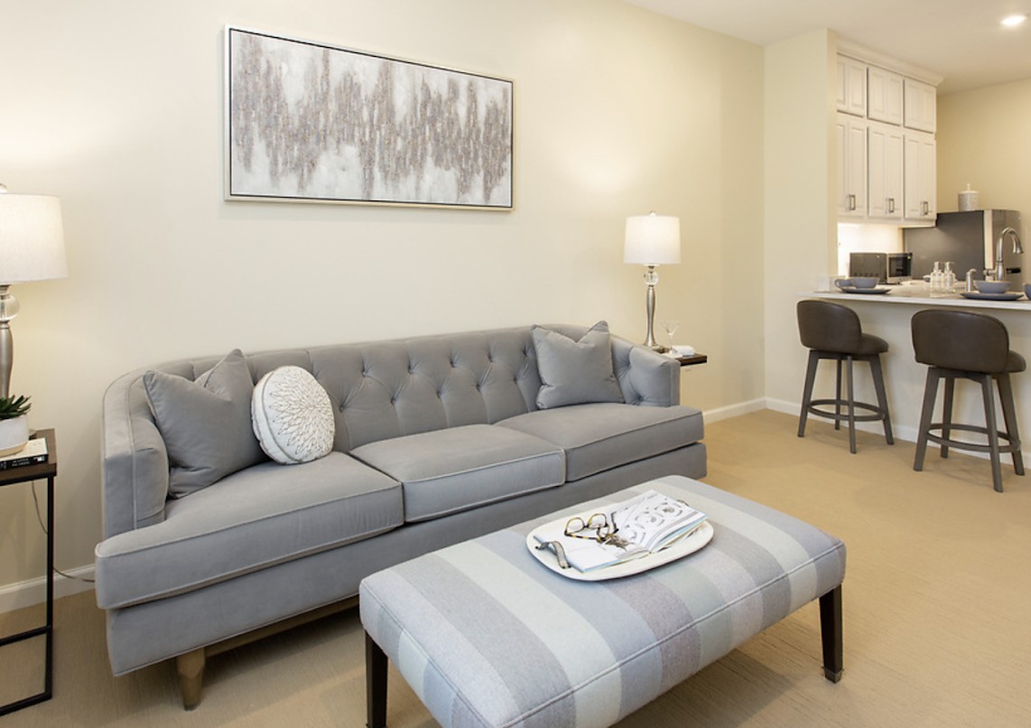 A modern living room with a gray sofa, striped ottoman, and elegant decor.