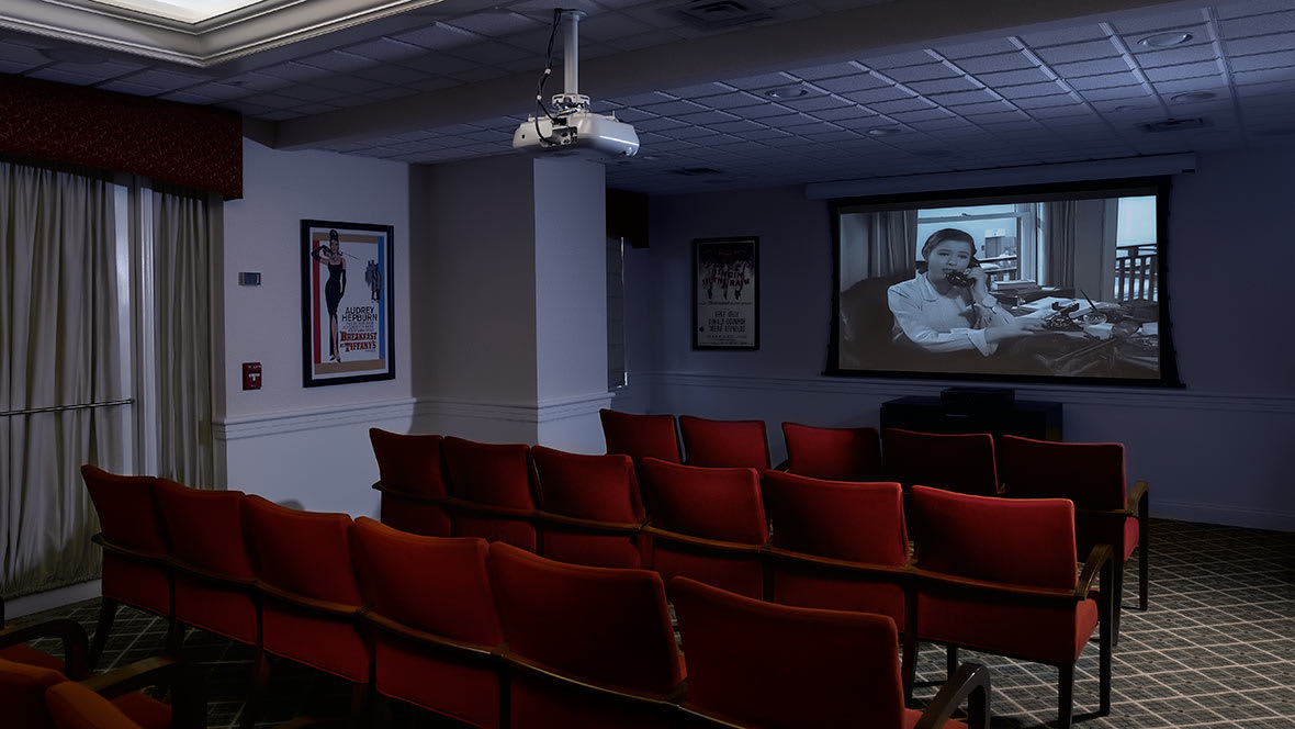 An empty movie theater with red seats and a film playing on the screen.