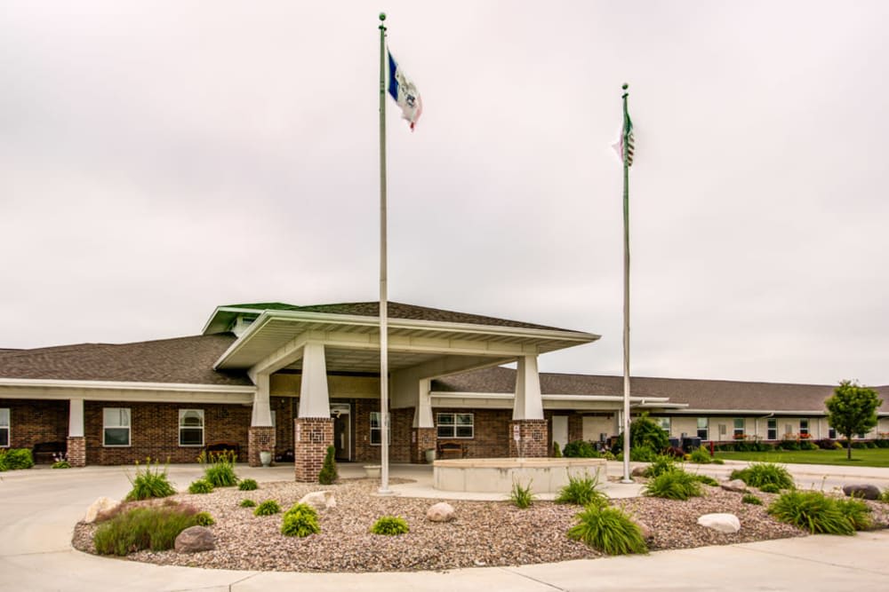 A single-story building entrance with flagpoles and landscaped surroundings under a cloudy sky.