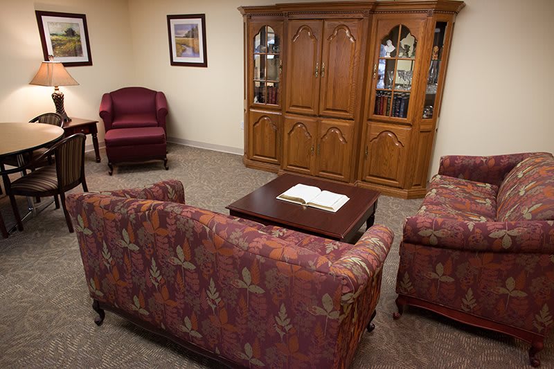 A cozy living room with patterned sofas, an armchair, a wooden cabinet, and a central coffee table.