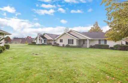 A suburban house with a large grassy lawn under a blue sky with clouds.