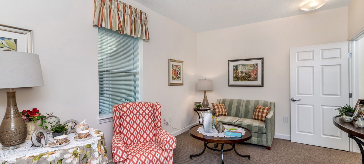 A cozy living room featuring a patterned armchair, striped sofa, and a classic coffee table with decorative items.