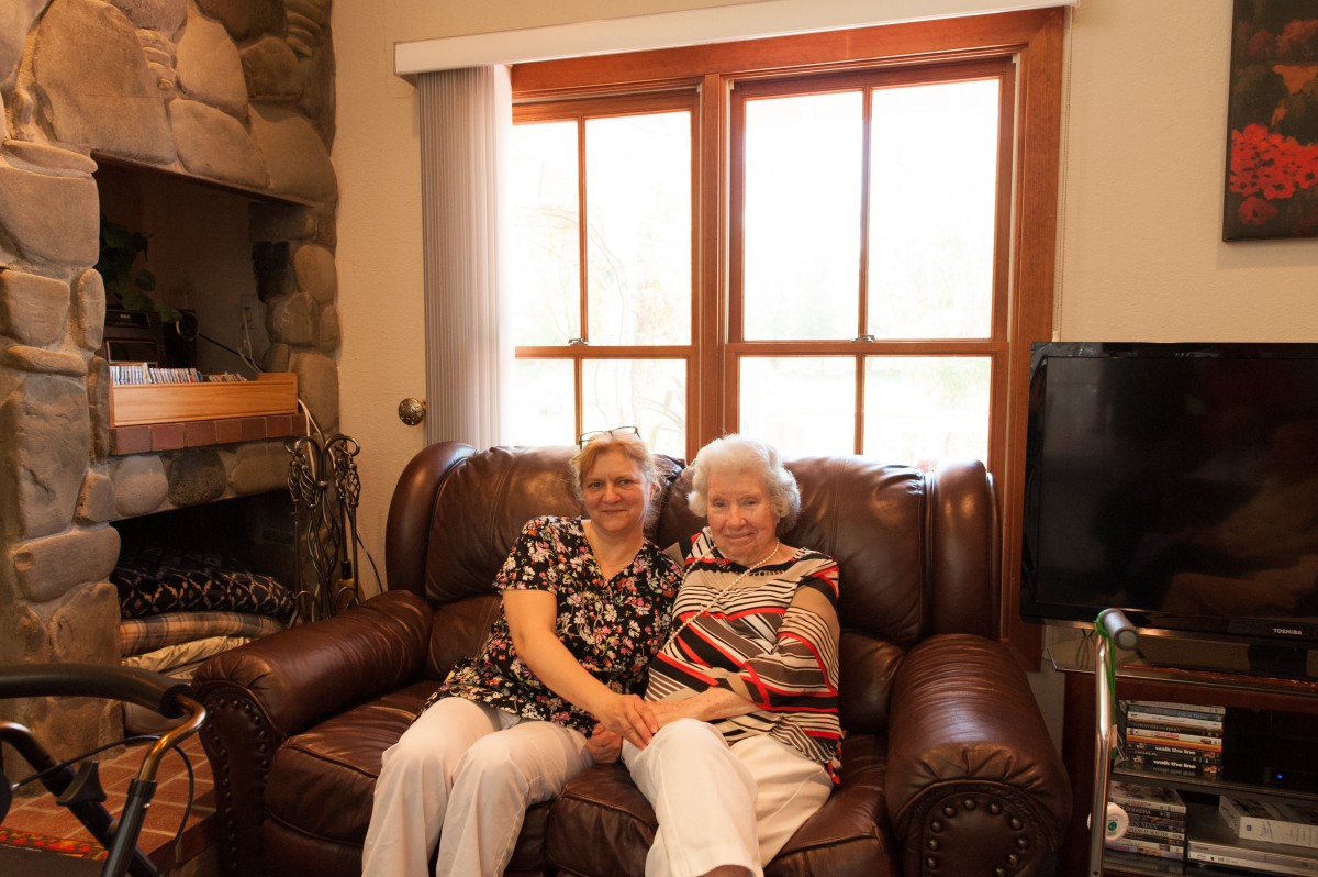 Two women sitting together on a couch, smiling in a cozy home setting.