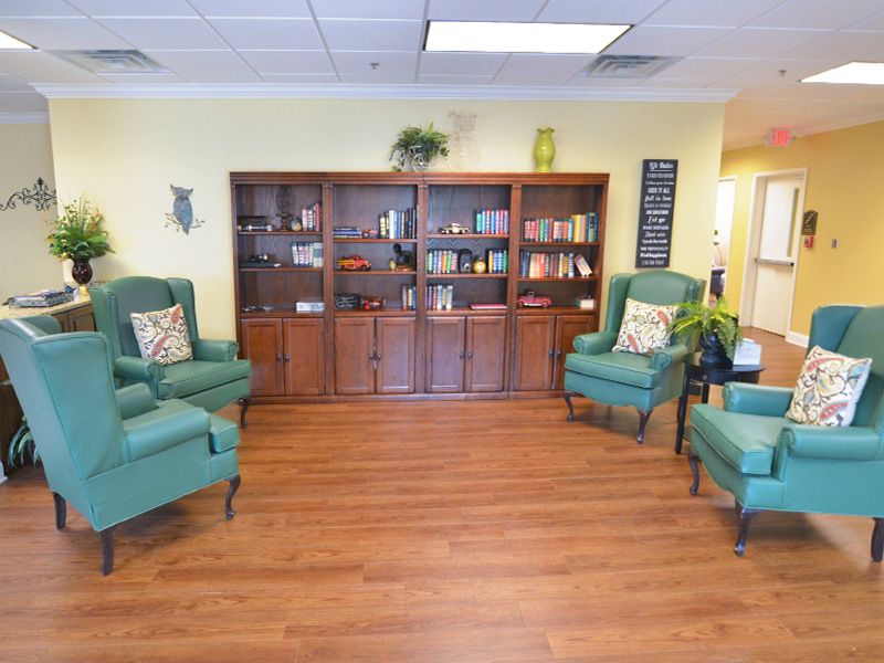 A cozy living room with armchairs, a bookshelf, and decorative plants on a wooden floor.