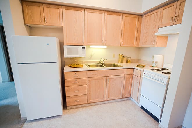A compact kitchen with wooden cabinets, a refrigerator, stove, microwave, and sink.