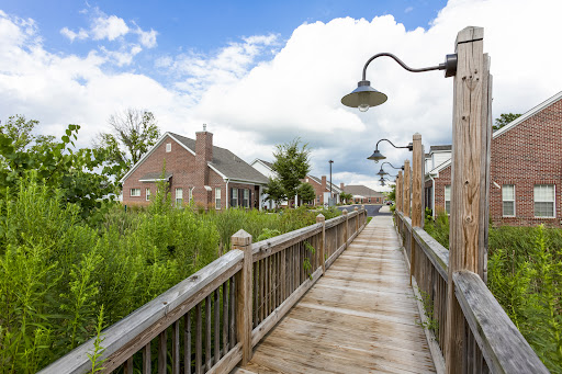A scenic wooden pathway lined with houses, leading through lush greenery under a partly cloudy sky.