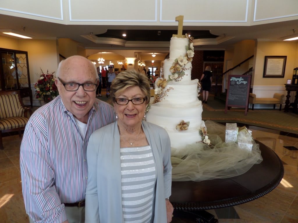 A couple posing in front of a large, decorative cake at an indoor event.