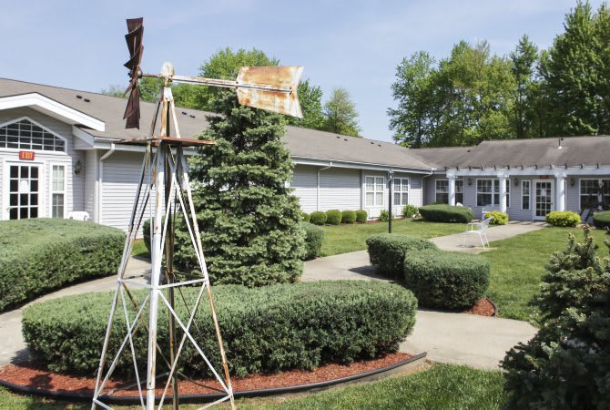 A well-manicured garden with a small windmill and neatly trimmed shrubs in front of a residential building.