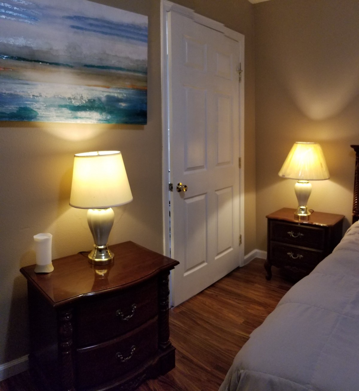 A cozy bedroom with two lamps on nightstands by a bed and a painting on the wall.