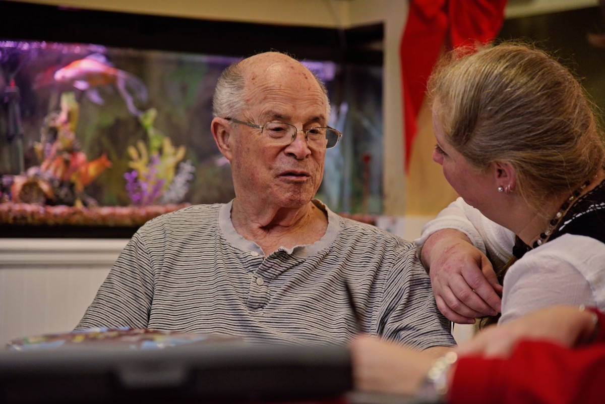 An elderly man and a woman are having a conversation indoors, near an aquarium.