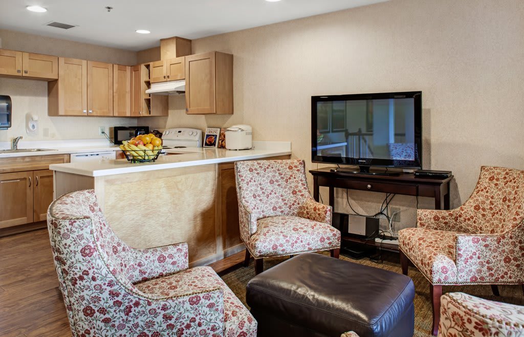 A cozy living room with a small kitchen area featuring floral patterned chairs and a TV.