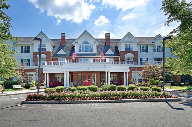 A picturesque residential building with flags displayed at the entrance and a well-maintained garden.