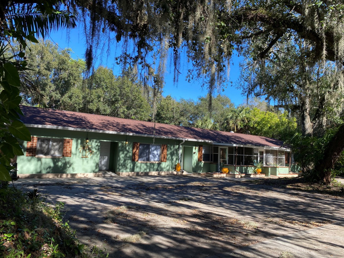 A serene green house under the shade of large trees on a sunny day.