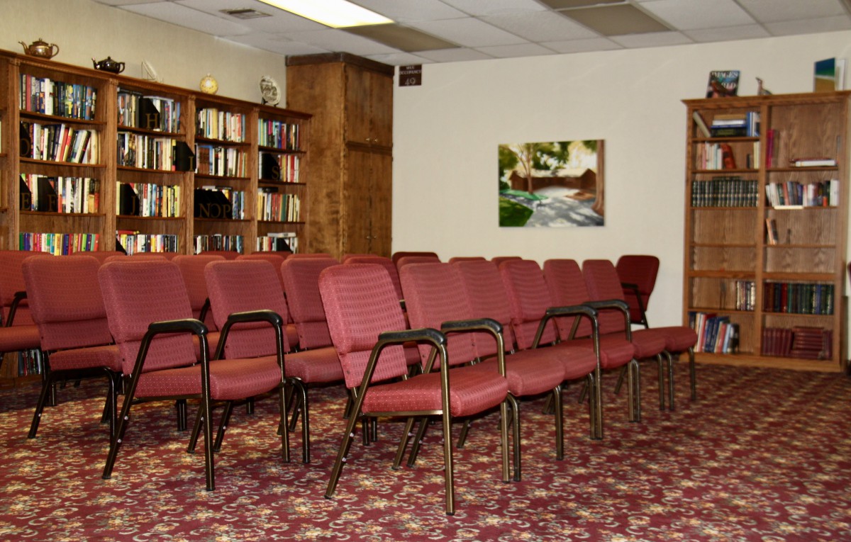 An empty meeting room with red chairs and a bookshelf filled with books.