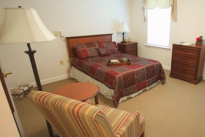 A cozy bedroom with a neatly made bed, bedside table, and a comfortable chair.