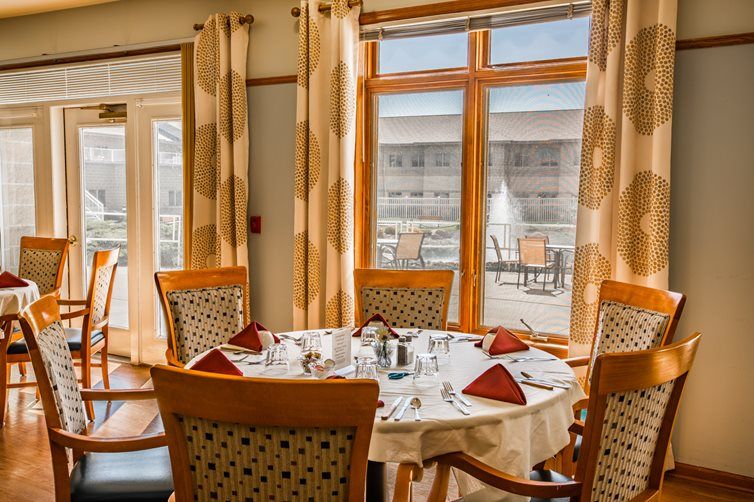 A cozy dining area with a round table set for a meal, surrounded by chairs and large windows.