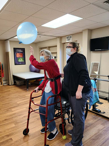 An elderly individual participates in a therapeutic exercise session while receiving assistance from a caregiver.