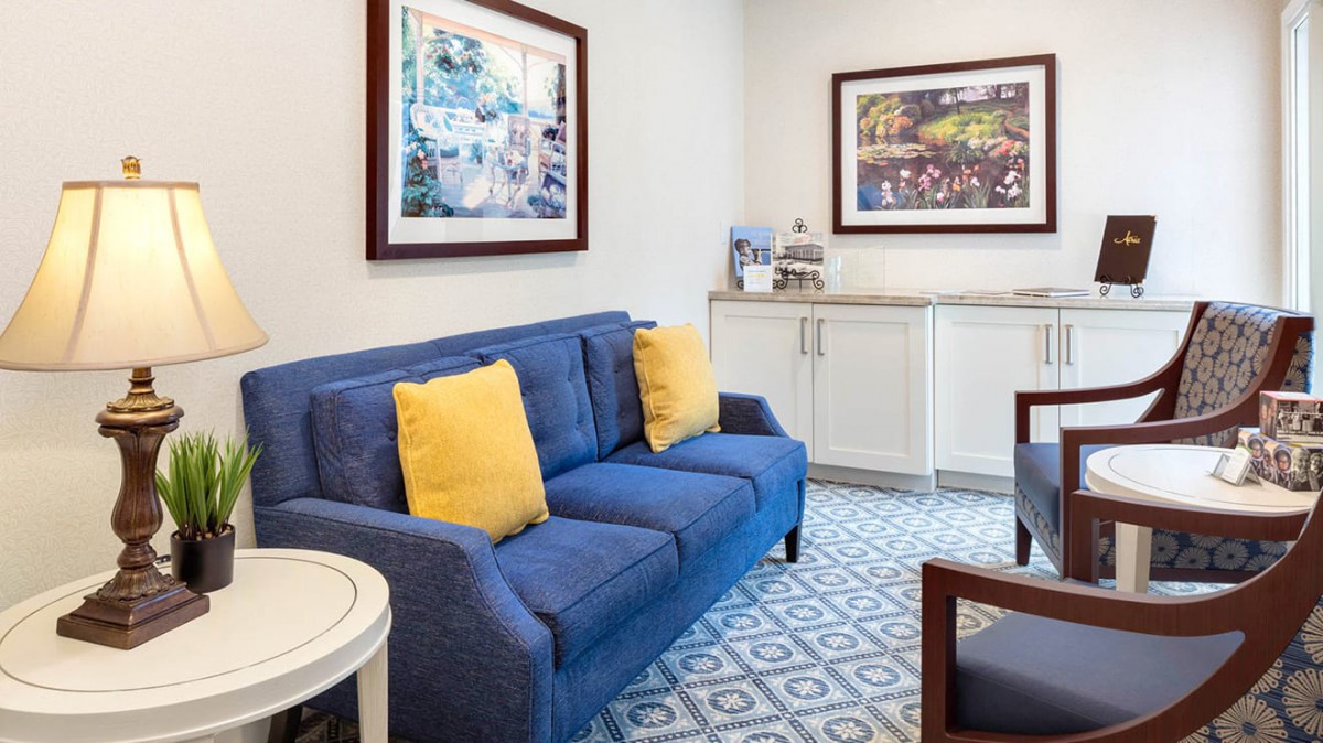 A cozy living room with a blue sofa and yellow pillows, complemented by artwork on the walls and a patterned carpet.