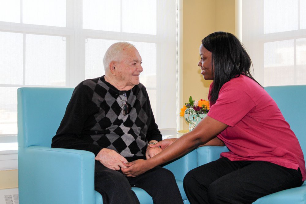 A caregiver offering support to an elderly man in a healthcare setting.