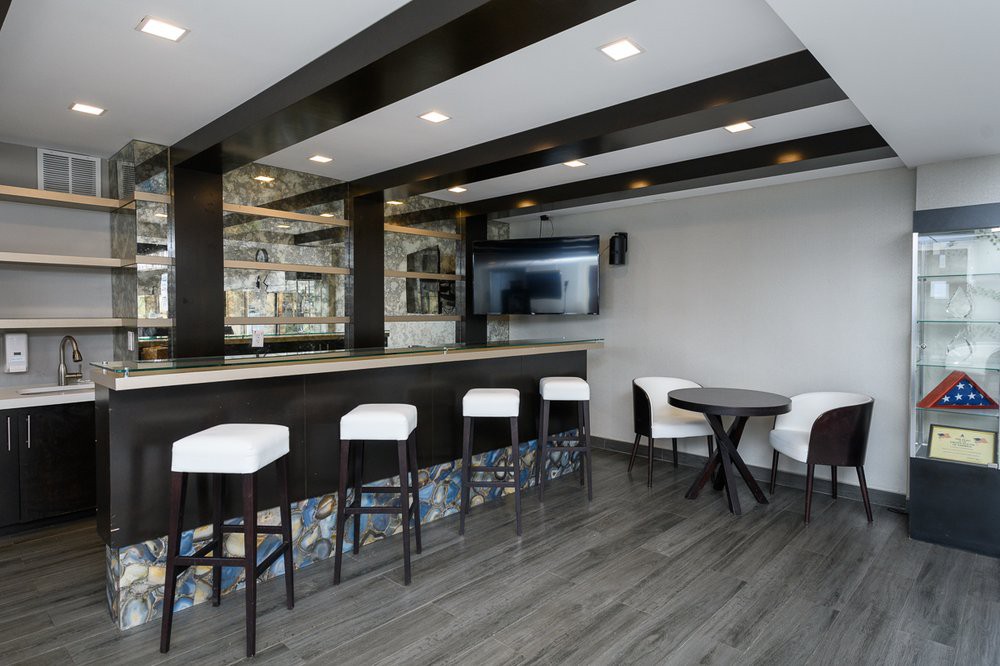 A modern bar area with sleek black and white decor, featuring a counter with stools and a television on the wall.