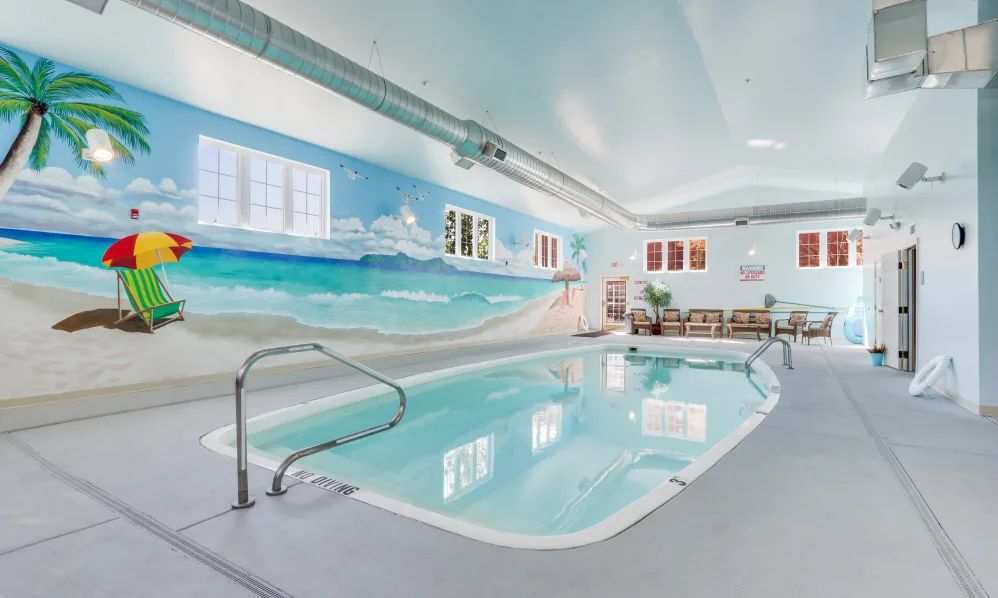 A serene indoor swimming pool with a vibrant beach-themed mural on the wall.