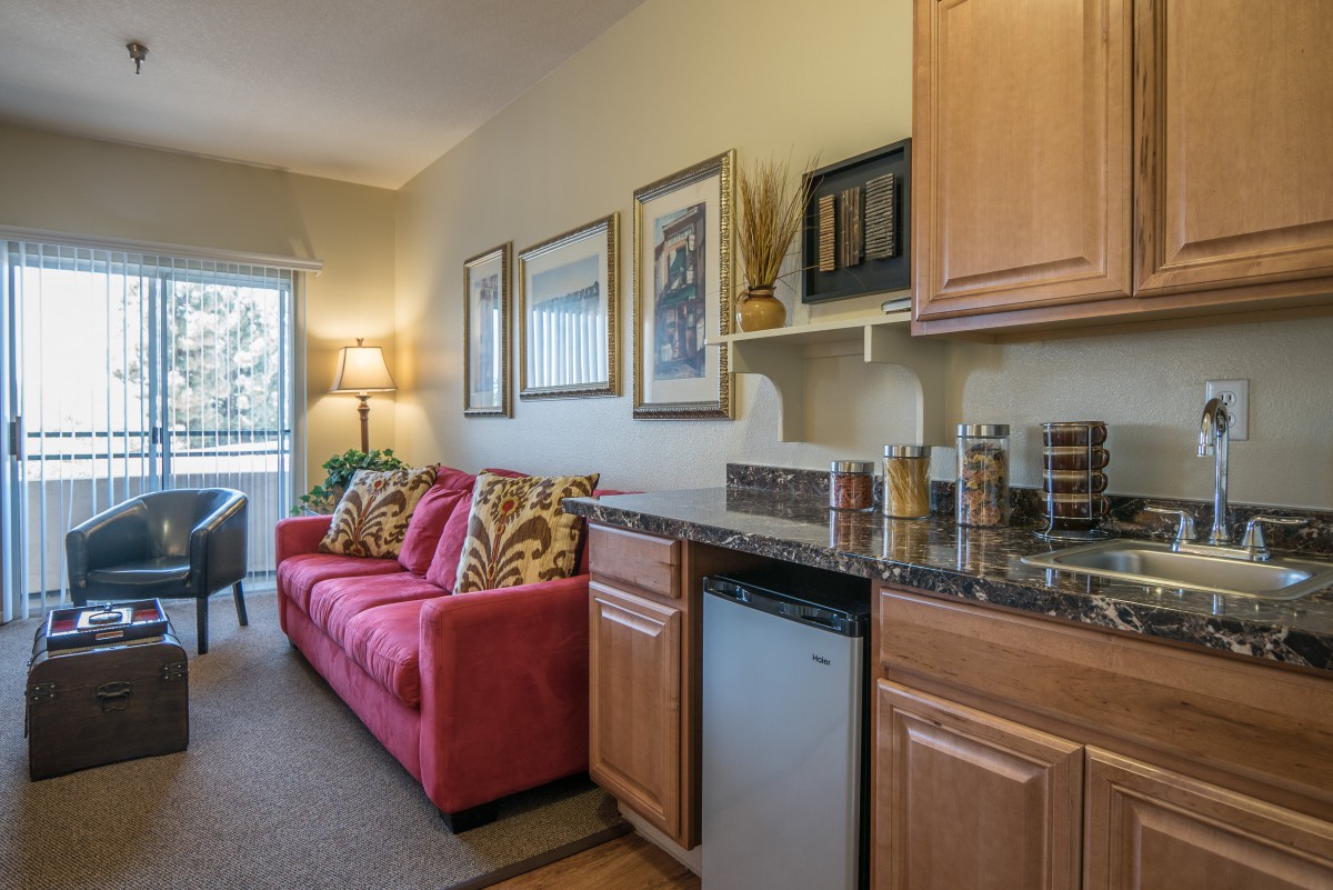 A cozy living area with a red sofa, kitchenette, and wall art in an apartment.
