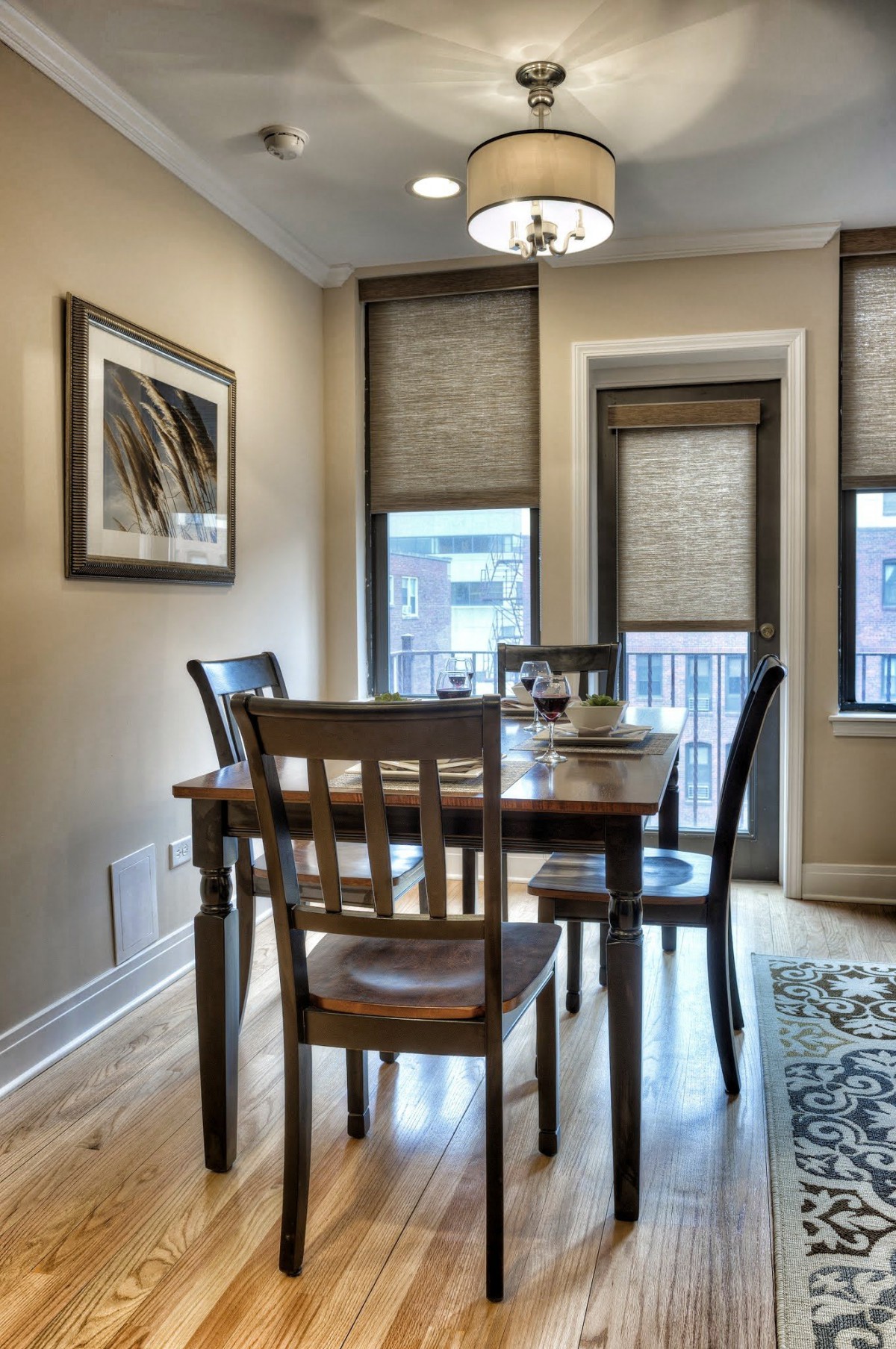 A cozy dining area featuring a wooden table and chairs with large windows adorned with blinds.
