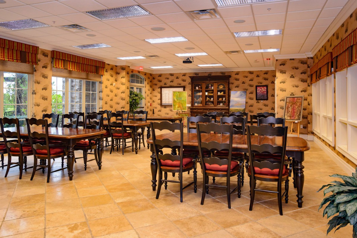 A spacious dining room with wooden tables and chairs arranged neatly, featuring warm lighting and decorative wall patterns.