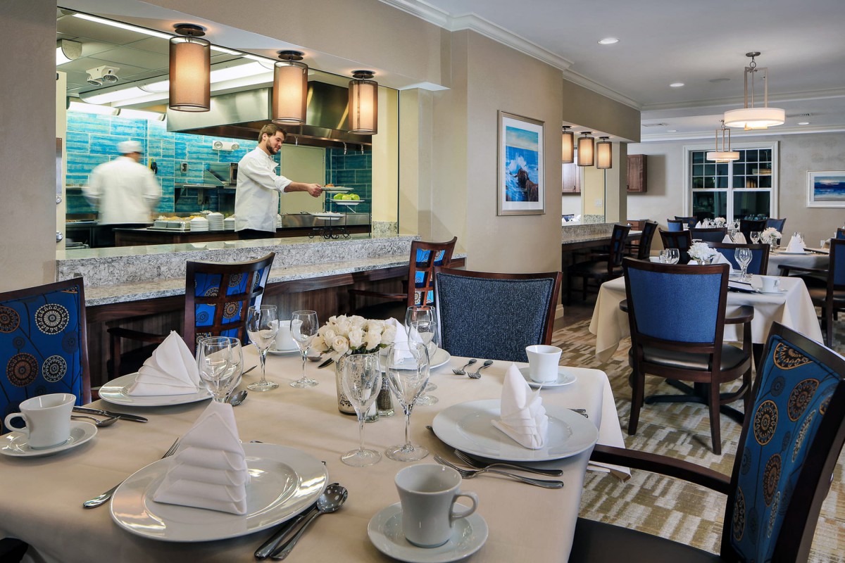 A well-arranged restaurant dining area with a view into the kitchen where a chef is at work.