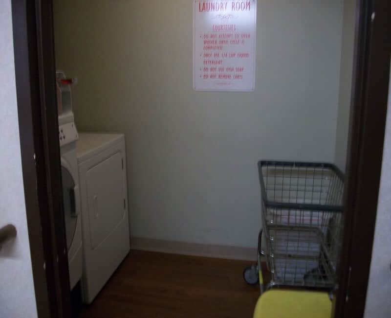A small laundry room with a washing machine, a laundry cart, and a sign on the wall.