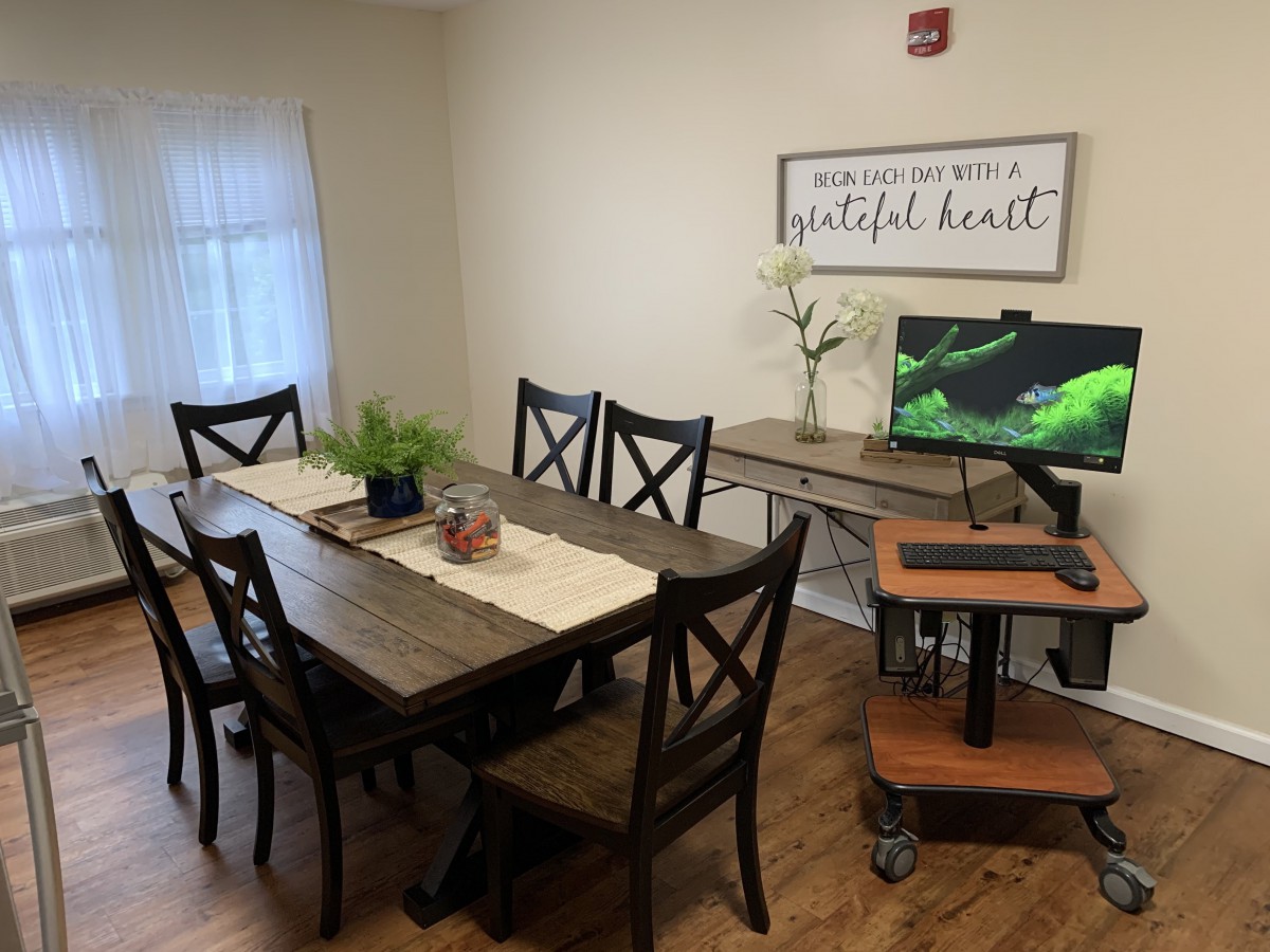 A cozy dining room with a wooden table, chairs, indoor plants, and a computer setup on the side.