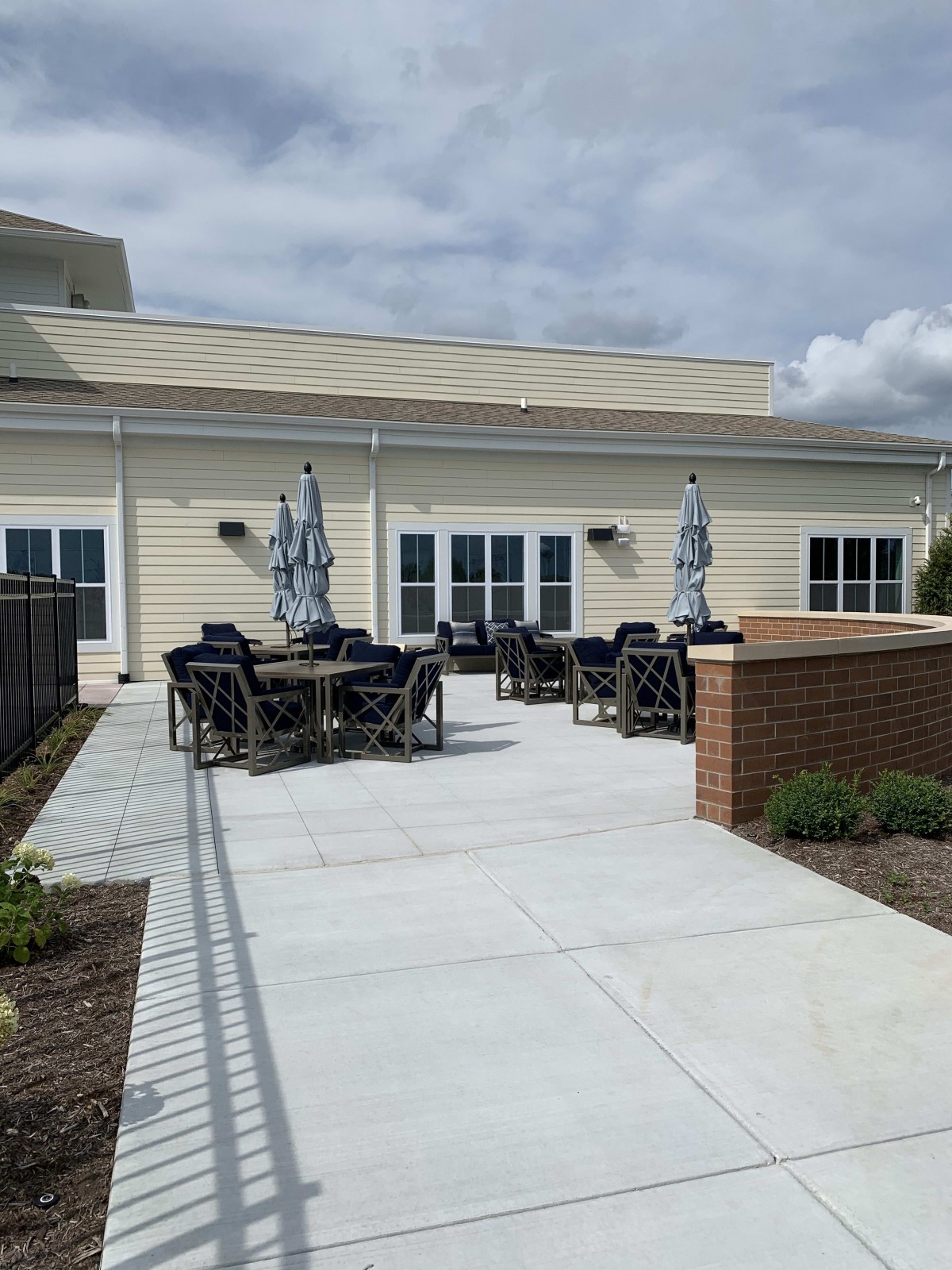 An outdoor patio area with tables, chairs, and umbrellas set against a building under a cloudy sky.