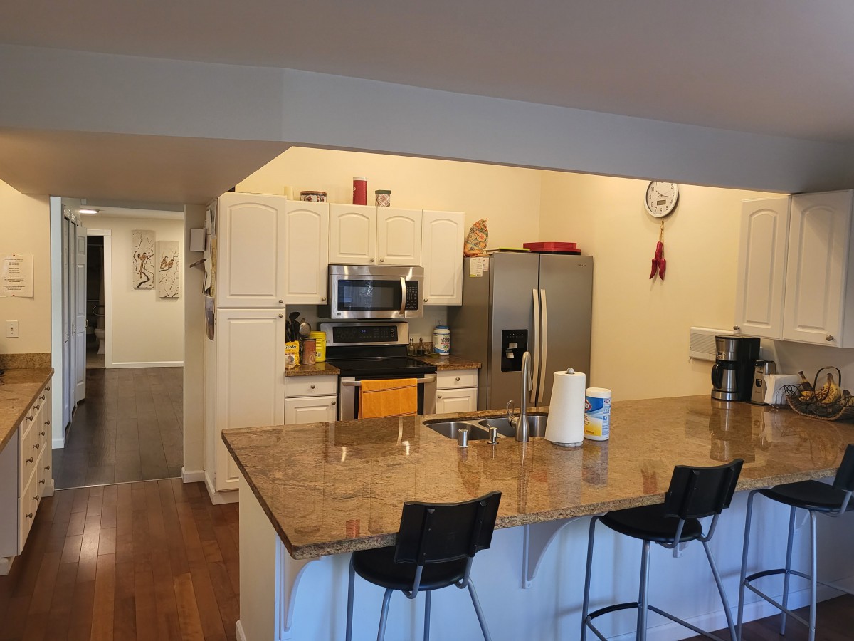 Modern kitchen with a large countertop and bar stools, featuring stainless steel appliances.