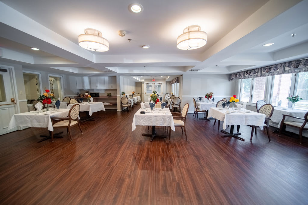 A well-lit dining area with elegantly set tables and chairs, featuring wooden flooring and modern decor.