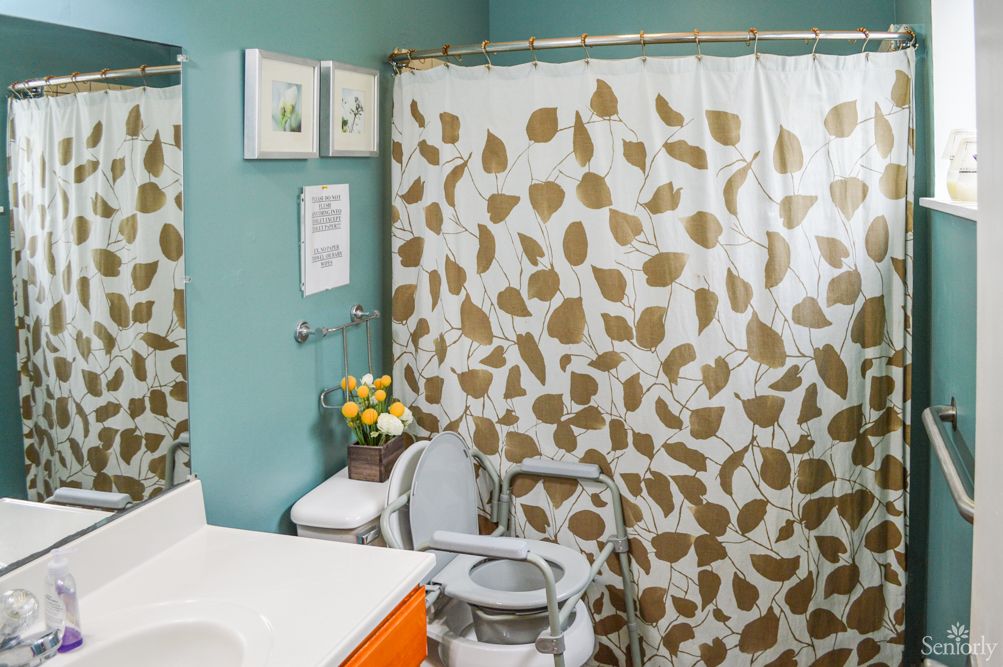 A bathroom with a leaf-patterned shower curtain and accessibility features.