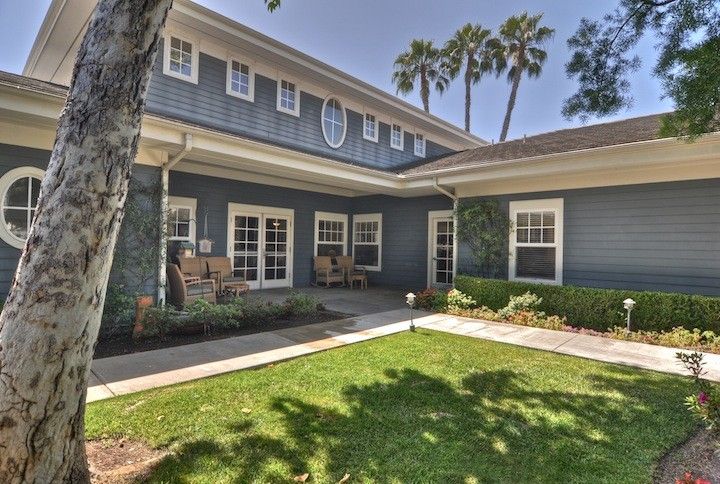 A two-story residential house with a well-kept lawn and surrounding palm trees.