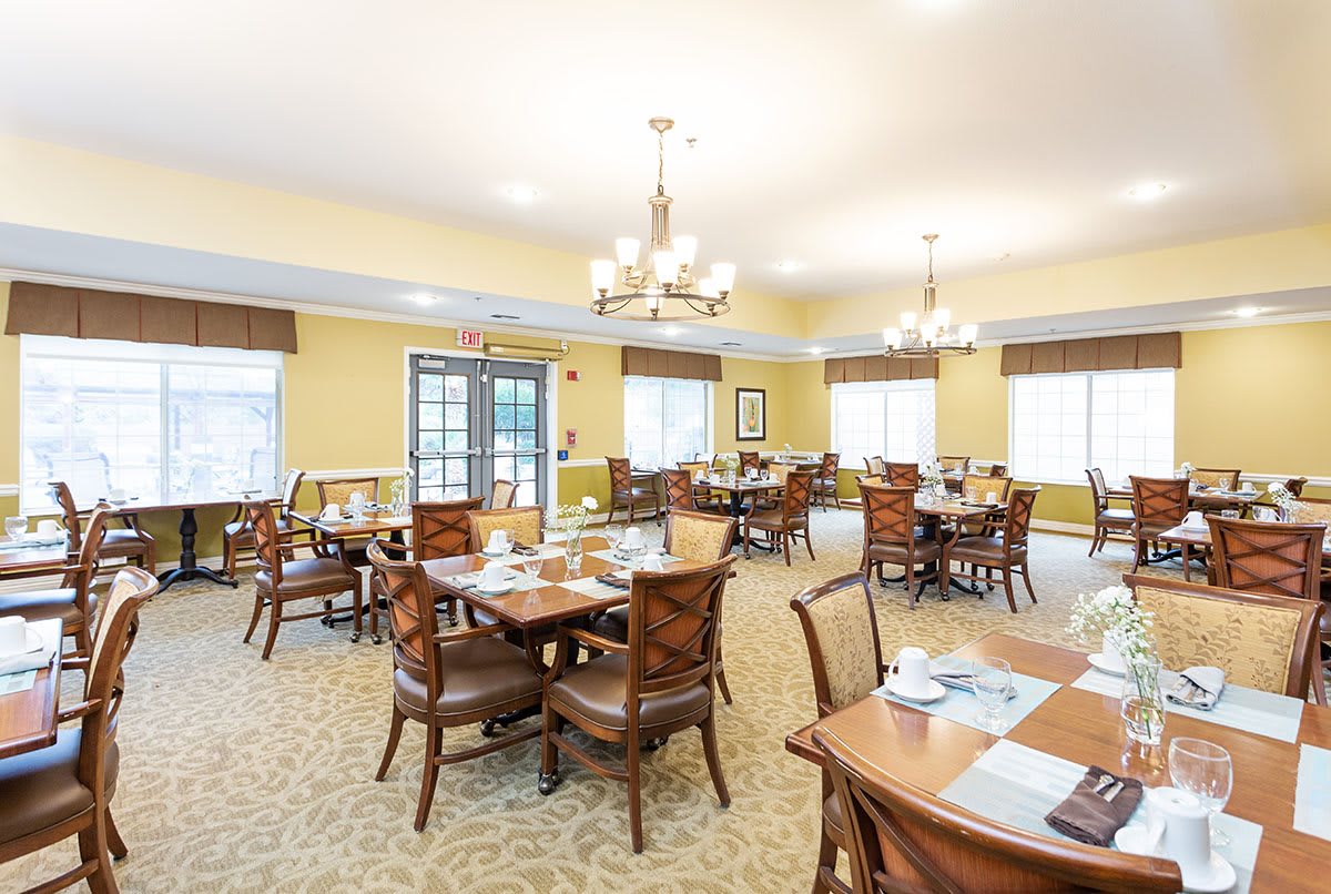A spacious and elegantly designed dining area with wooden tables and chairs, set for a meal.