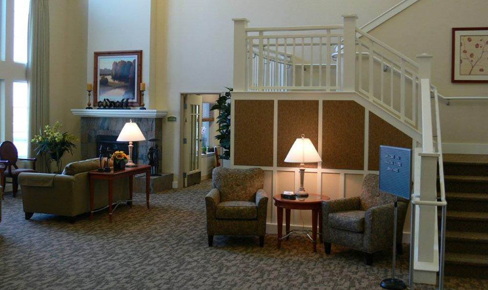 A cozy lobby interior featuring comfortable seating, warm lighting from lamps, and a staircase.