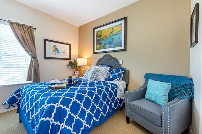 A cozy bedroom with blue patterned bedding and decorative pillows, complemented by wall art and a comfortable armchair.