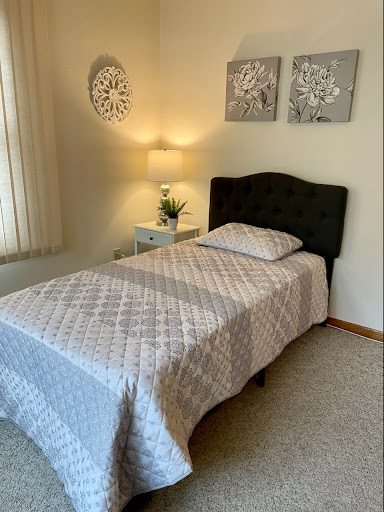 A cozy and well-decorated bedroom featuring a single bed with a soft quilt, accompanied by stylish wall art and a bedside lamp.