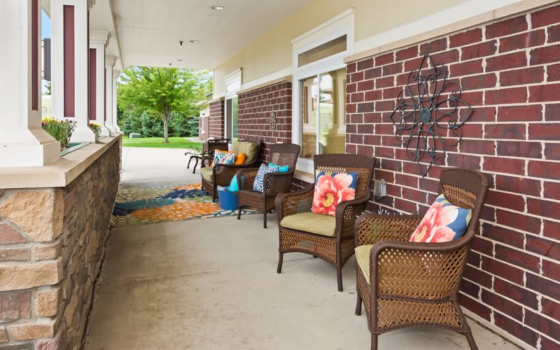A cozy outdoor patio with wicker chairs adorned with colorful pillows, set against a brick wall.