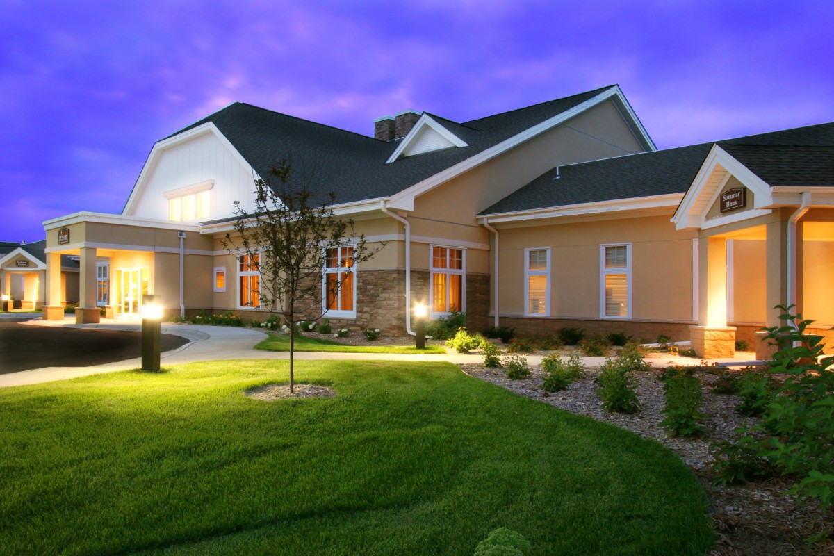 A well-lit suburban house with a manicured lawn during dusk.