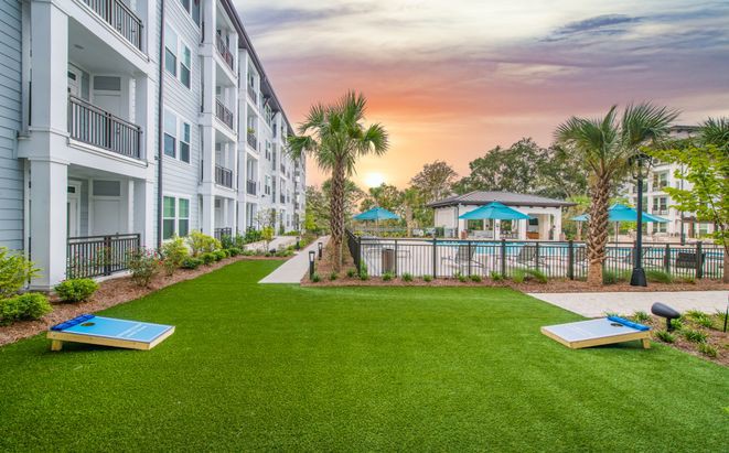 A scenic view of a residential apartment complex with a well-maintained lawn, palm tree, and swimming pool at sunset.