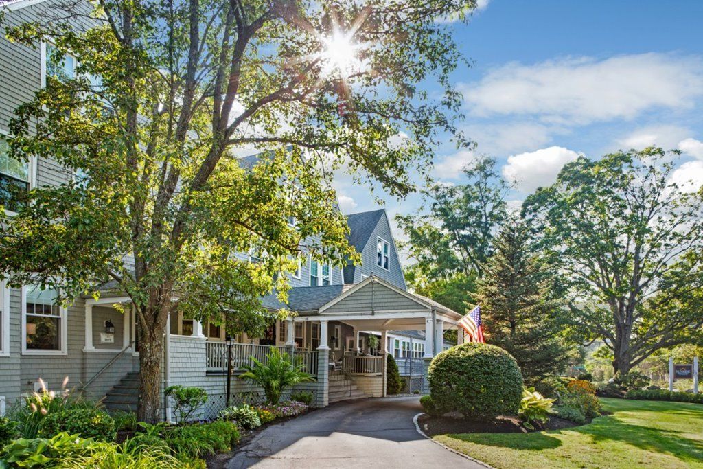 A picturesque house with sunlight filtering through trees, surrounded by a lush garden and driveway.