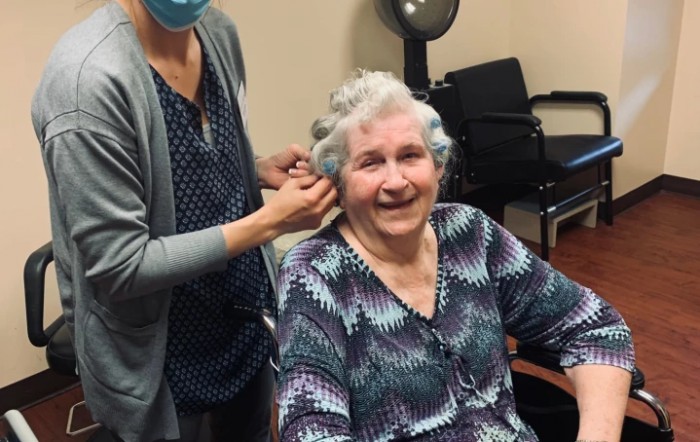 An elderly woman smiling while getting her hair styled at a salon.