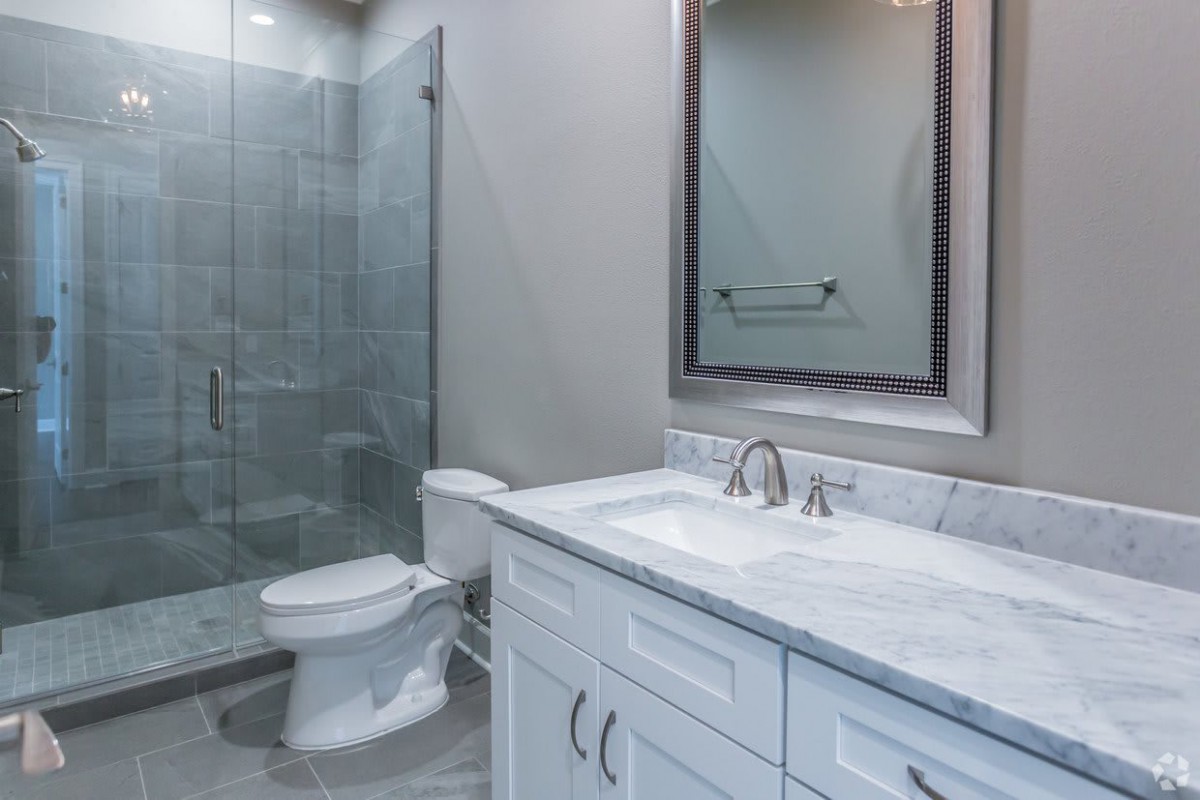 A modern bathroom with a glass shower, sink, and white cabinetry.