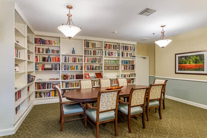 A cozy library reading room featuring a long wooden table surrounded by chairs, with bookshelves lining the walls.