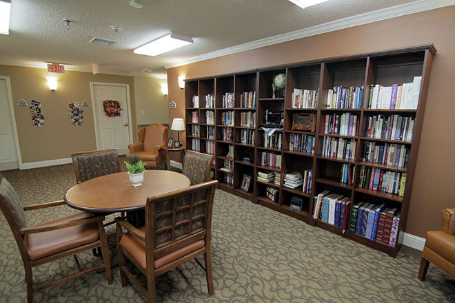 A cozy library room with shelves full of books, a round table, and chairs.