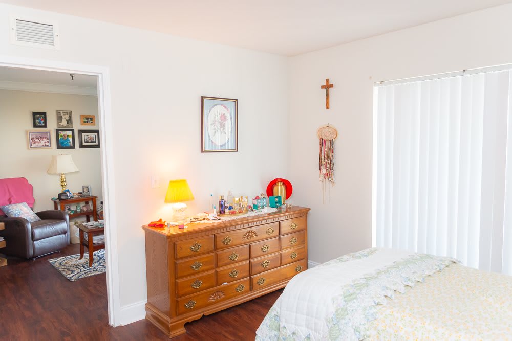 A cozy bedroom with a wooden dresser adorned with various items, alongside a lamp and wall decor.