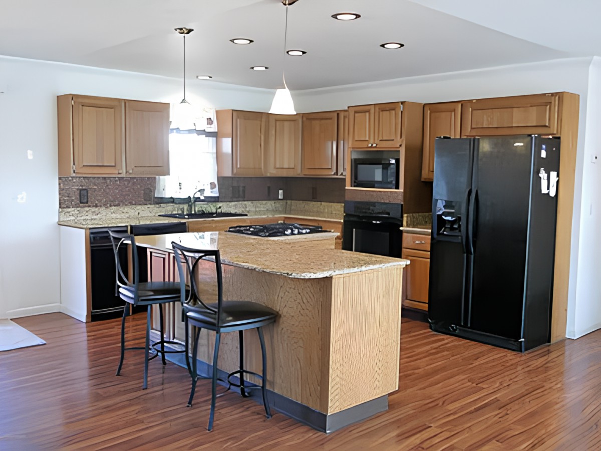 A modern kitchen with wooden cabinets, an island with bar stools, and black appliances.